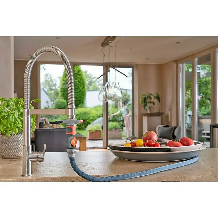 Gardena Gartenschlauch Liano Xtreme Set mit Hahnverbinder - Schlauch, Bewässerungsbrause, Indoor-Schlauchverbinder mit Regulierventil, Wasserstop, Hahnverbinder - Nahaufnahme eines Gardena Wasserhahns mit flexiblem Schlauch, der auf einer Küchentheke mit frischem Gemüse und Kräutern liegt.