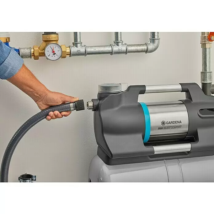 Gardena Hauswasserwerk 6300 Silent Comfort - 1.050 W, Max. Fördermenge: 6.300 l/h, Max. Druck: 4,9 bar - Eine Hand verbindet einen grauen Schlauch mit einer grauen und Edelstahl Gardena 5600 Silent Comfort Wasserpumpe, Teil eines Rohrsystems.