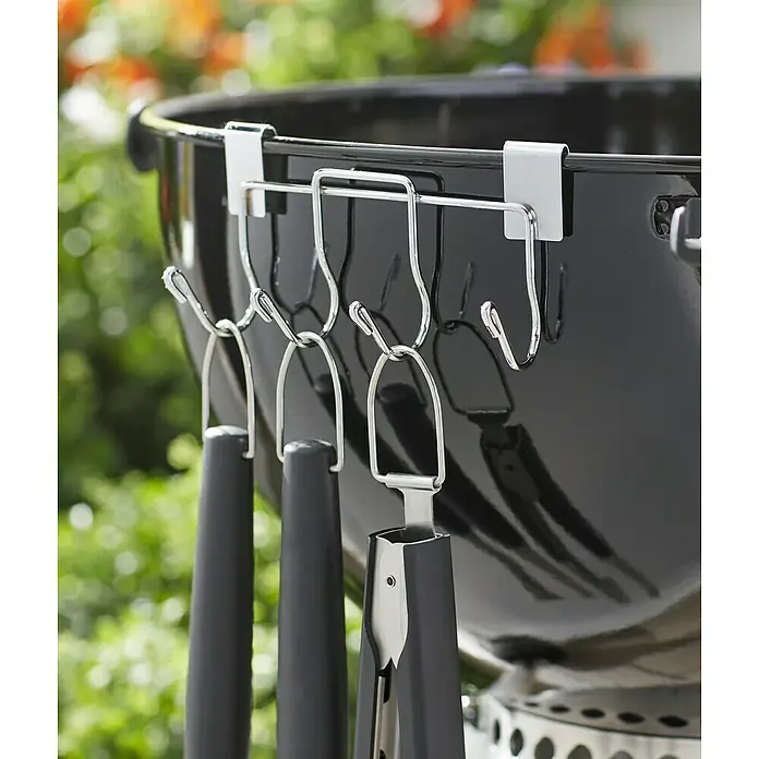 Weber Grillbesteckhalter - Stahl - Detailaufnahme eines Grillbesteckhalters mit Zange und Wender am schwarzen Kugelgrill im Freien.