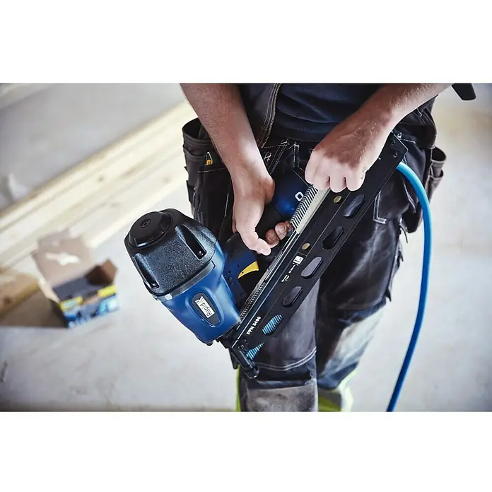 Rapid Druckluft-Streifennagler Rapid PRO PFN3490 - Betriebsdruck: 5 bar - 8 bar, Geeignet für: Streifennägel 50 - 90 mm - Eine Nahaufnahme eines Rapid PPN3490 Akku-Nagelgeräts, das von einer Person in Arbeitskleidung gehalten wird, mit einem blauen Luftschlauch.
