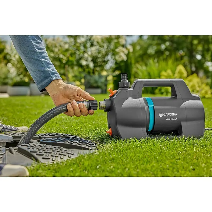Gardena Gartenpumpen-Set 4200 Silent600 W, Max. Fördermenge: 4.200 l/h - Eine Person schließt einen Schlauch an eine Gardena 4200 Silent Gartenpumpe an. Die Pumpe steht auf einem grünen Rasen.