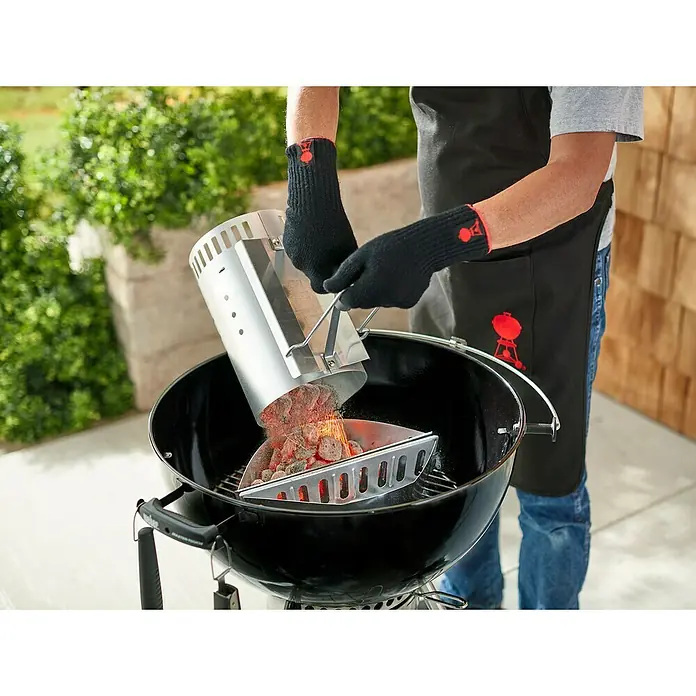 Weber Anzündkamin Rapidfire - Ø x H: 19 x 30 cm - Das Foto zeigt einen Mann, der mit dem Anzündkamin glühende Kohlen in einen Weber Grill schüttet.