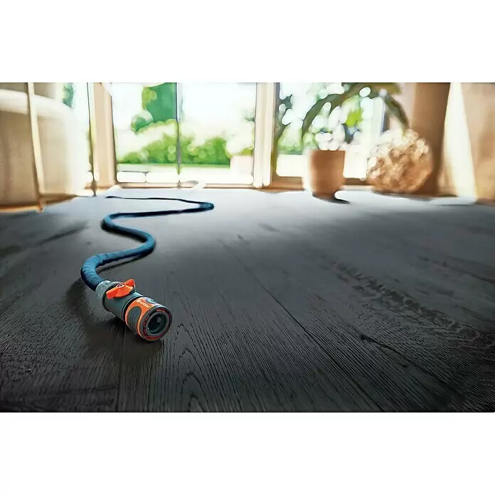 Gardena Gartenschlauch Liano Xtreme Set mit Hahnverbinder - Schlauch, Bewässerungsbrause, Indoor-Schlauchverbinder mit Regulierventil, Wasserstop, Hahnverbinder - Ein orange-grauer Gardena Schlauchverbinder mit blauem Schlauch auf dunklem Holzboden, der zu hellen Fenstern und einem Garten führt.