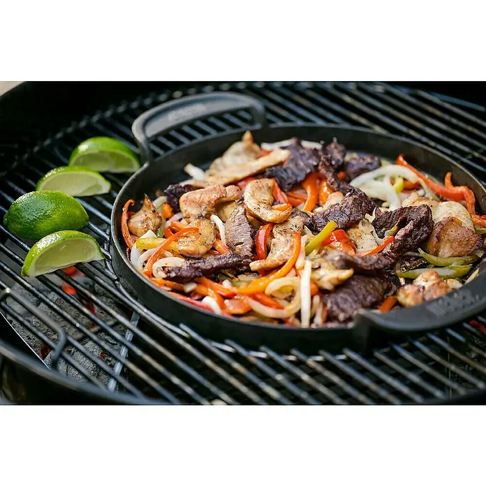 Weber Gourmet BBQ System Plancha - Diámetro: 38,6 cm, Hierro fundido esmaltado - Una sartén de fajitas y limas en una parrilla. La comida consta de carne y verduras, incluyendo pimientos y cebollas.