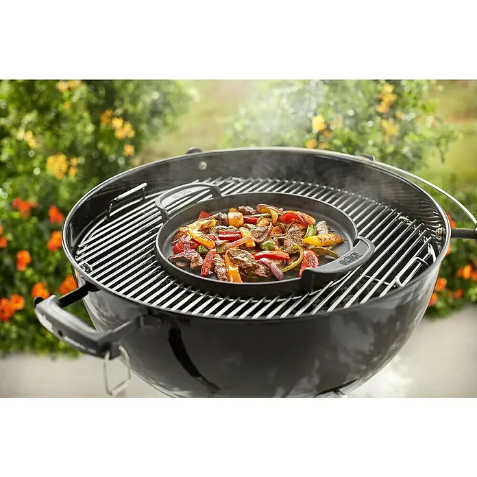 Weber Gourmet BBQ System Plancha - Diámetro: 38,6 cm, Hierro fundido esmaltado - Una barbacoa Weber con una plancha en la parrilla, cocinando fajitas, rodeada de naturaleza verde al fondo.