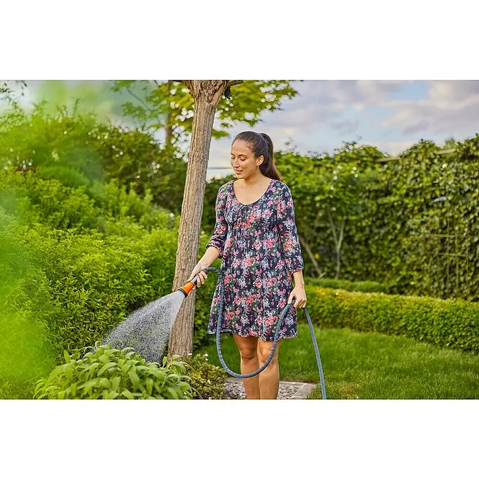 Gardena Gartenschlauch Liano Xtreme Set - Schlauch, Wasserstop, Schlauchverbinder, 2x Hahnverbinder, Bewässerungsbrause - Eine Frau gießt ihren Garten mit einem orangefarbenen Gartenschlauch. Die Gießbrause ist mit einer praktischen Spritzpistole ausgestattet.