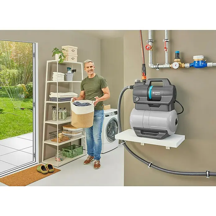Gardena Hauswasserwerk 3800 Silent - 600 W, Max. Fördermenge: 3.800 l/h, Max. Druck: 3,9 bar - Abbildung einer Gardena Hauswasseranlage auf einem Regal mit einem Mann im Hintergrund, der einen Wäschekorb hält.