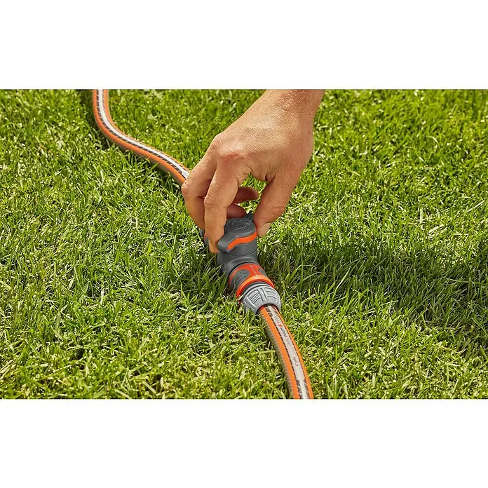 Gardena Schlauchkupplung mit Regulierventil - Frostbeständig, Geeignet für: Gartenschläuche - Ein Mann schließt einen Gardena-Wasserhahn an einen Gartenschlauch an, der auf einem saftig grünen Rasen liegt.