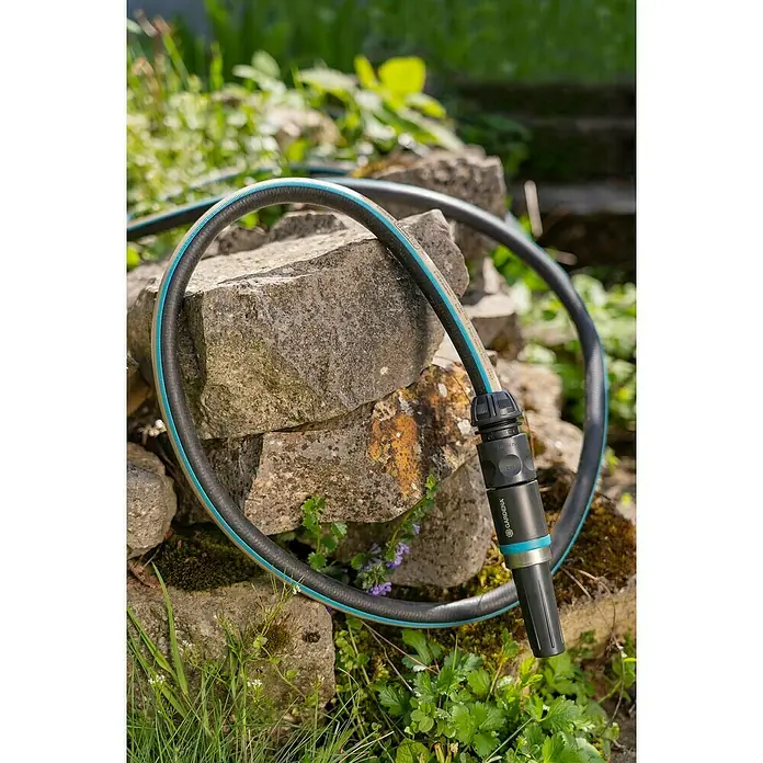 Gardena EcoLine Gartenschlauch Set - 20 m, Ausstattung: Anschlussstücke - Gartenschlauch mit GARDENA-Anschlussstück auf Steinen im Garten. Der Schlauch ist schwarz mit einem blauen Streifen.