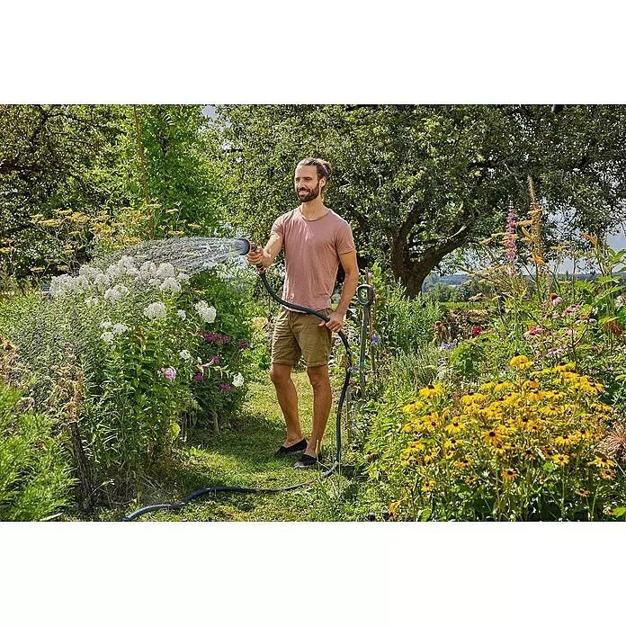 Gardena Gartenschlauch Liano Xtreme Set - 20 m, Schlauchdurchmesser: 19 mm - Ein Mann bewässert mit Gartenschlauch und Spritze bunte Blumen in einem üppigen Garten.