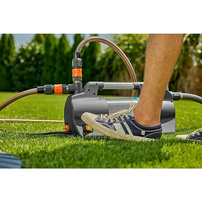 Gardena Gartenpumpe 5600 Silent+900 W, Max. Fördermenge: 5.600 l/h - Eine Gardena Gartenpumpe mit Schlauchanschluss auf Rasen, betätigt durch einen Fuß, ideal für Gartenbewässerung und Wasserförderung.