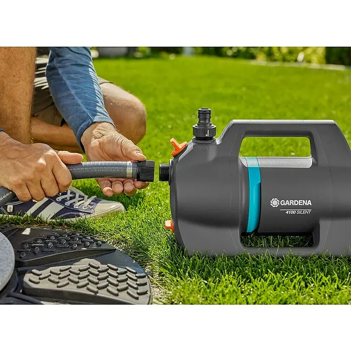 Gardena Gartenpumpen-Set 4100 Silent Saugschlauch550 W, Max. Fördermenge: 4.100 l/h - Eine Gardena 4100 Silent Gartenpumpe wird an einen Gartenschlauch angeschlossen. Sie ist grau mit türkisfarbenen Akzenten.