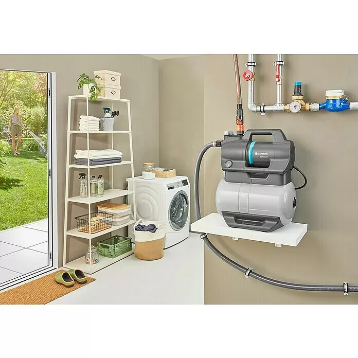 Gardena Hauswasserwerk 3800 Silent - 600 W, Max. Fördermenge: 3.800 l/h, Max. Druck: 3,9 bar - Graue Gardena 3800 Silent Wasserpumpe auf einem Regal im Hauswirtschaftsraum, an Rohre für die Gartenbewässerung angeschlossen, durch Tür sichtbar.