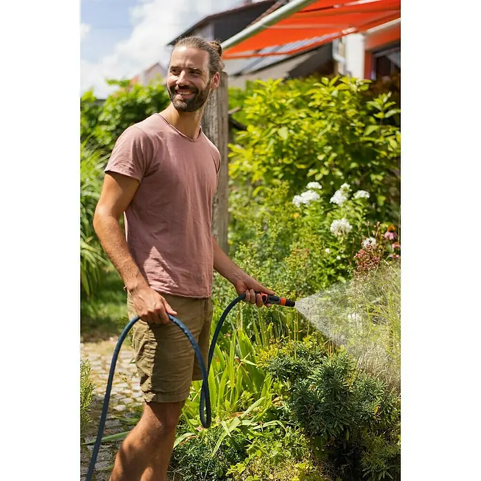 Gardena Gartenschlauch Liano Xtreme Set mit Wandschlauchhalter - Länge: 15 m - Ein Mann gießt mit einem Gartenschlauch seine Pflanzen im Garten. Der Schlauch ist blau und hat einen orangefarbenen Sprühkopf.
