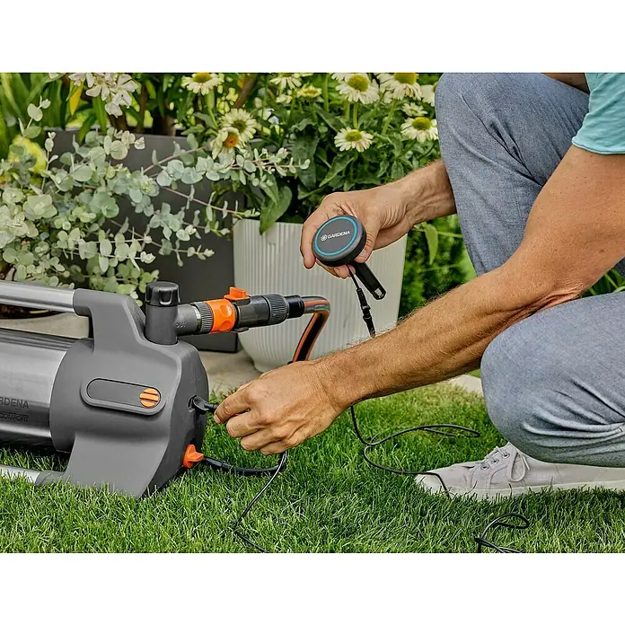 Gardena Gartenpumpe 6500 SilentComfort1.300 W, Max. Fördermenge: 6.500 l/h - Ein Mann schliesst eine graue Gardena-Gartenpumpe auf einem Rasen an. Das Gerät wird für die Gartenbewässerung vorbereitet.