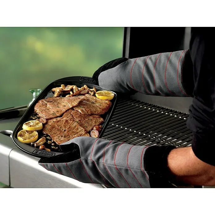 Weber Grillplatte - L x B: 40 x 22 cm - Ein Mann, der mit Weber Grillhandschuhen eine Platte mit gegrilltem Fleisch, Zitrone und Pilzen über einen Grill hält.