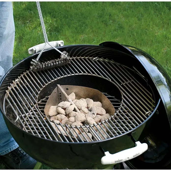 Weber Gourmet BBQ System Grillrost - L x B: 56,61 x 54,61 cm, Durchmesser: 57 cm, Verchromter Stahl - Ein Holzkohlegrill wird mit einem Reinigungsbürste gesäubert, während ein Anzündkamin voller Grillkohle auf dem Rost steht.