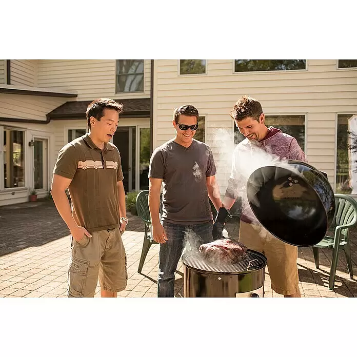 Weber Räucherofen Smokey Mountain Cooker - Durchmesser Grillfläche: 47 cm, Schwarz - Drei Männer stehen um einen schwarzen zylindrischen Smoker-Grill, in dem ein großes Stück Fleisch räuchert und Rauch aufsteigt.