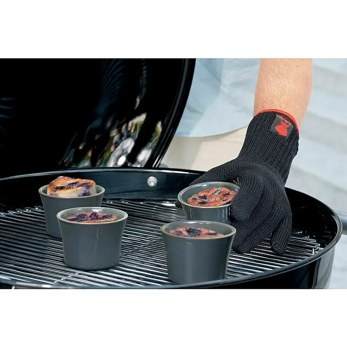 Weber Grillhandschuhe - Sonstiges, Größe S/M - Grillhandschuh, der einen Auflauf auf einem Grill hält.