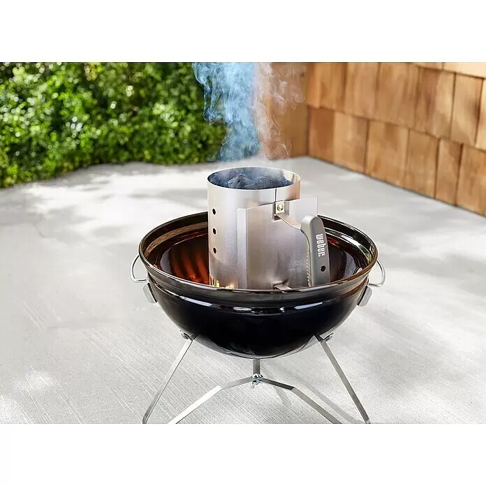 Weber Anzündkamin - B x T x H: 14,5 x 26,5 x 20,5 cm - Schwarzer Weber Kohlegrill mit silbernem Anzündkamin voller rauchender Holzkohle, bereit zum Grillen im Freien.