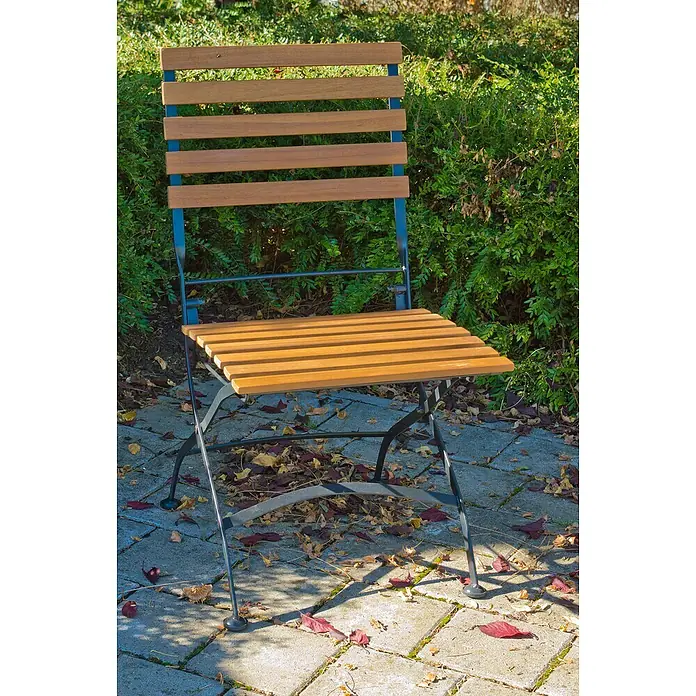 Acamp Gartenmöbel-Set Lindau - 4 -tlg., Akazie, Eisen, Braun, Stuhl ohne Armlehne - Gartenstuhl mit Holzlatten und Metallgestell auf einem gepflasterten Untergrund mit Blättern.