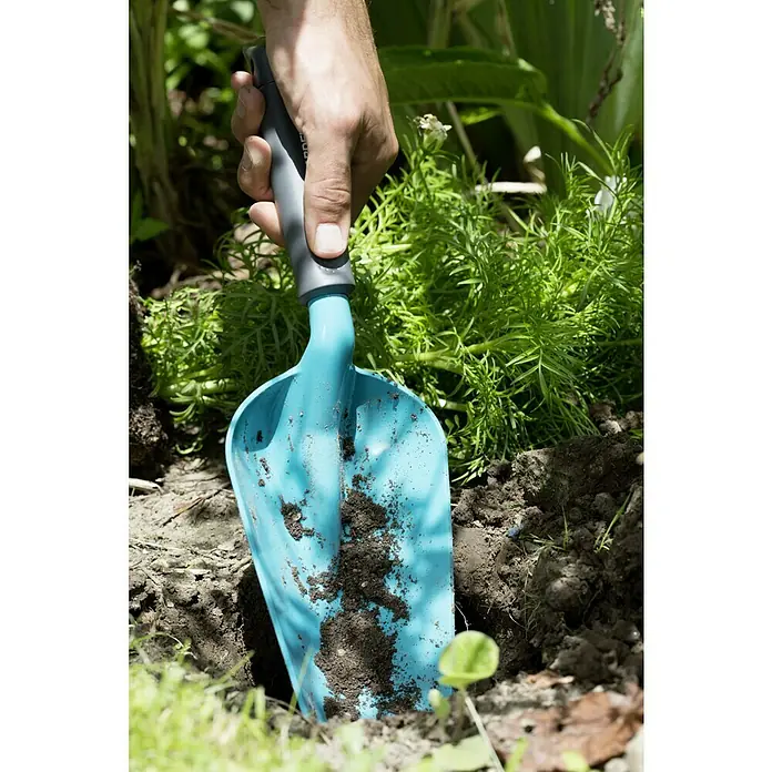 Gardena Classic Blumenkelle Groß - Stahl - Helle blaue Pflanzkelle mit grauem Griff wird in dunkle Erde gedrückt, um das Einpflanzen zu erleichtern.
