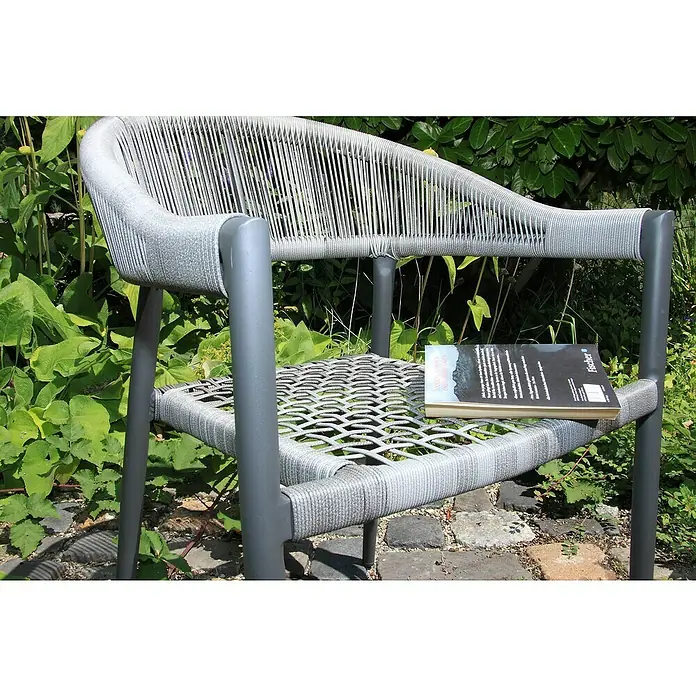 Acamp Stapelsessel Brooklyn - 4 Stk., Aluminium, Polyester, Stapelbar, Dunkelgrau, B x T x H: 58 x 56 x 78 cm - Buch auf einem grauen Rattansessel im Garten. Der Sessel ist hellgrau und aus Rattan gefertigt und steht auf einem gepflasterten Boden.