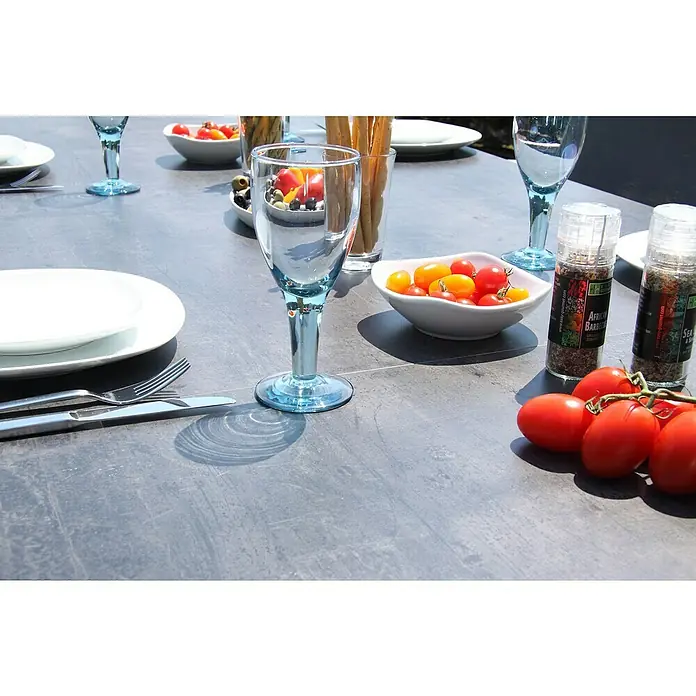 Acamp Gartenmöbel-Set Urban/Extensio - 5 -tlg., Aluminium, HPL, Textil, Klappbar, Anthrazit - Ein Esstisch im Freien mit blauen Gläsern, Tellern, Besteck, Tomaten und Gewürzen, ideal für Mahlzeiten im Freien.
