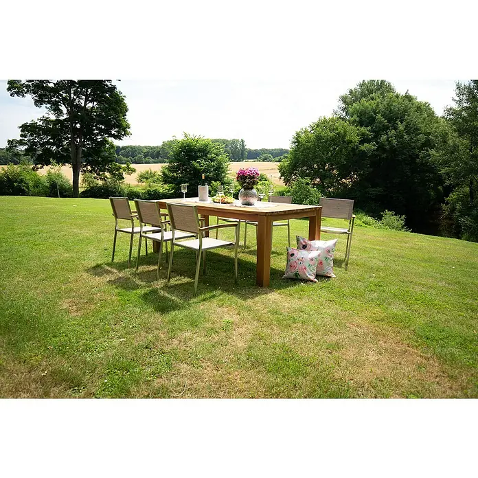 Acamp Gartenmöbel-Set Skye/Old Java - 7 -tlg., Aluminium, Akazie, Braun, Stapelbar - Im Freien steht ein Holztisch mit Stühlen, dekoriert mit Blumen und Getränken, umgeben von einer grünen Rasenfläche.