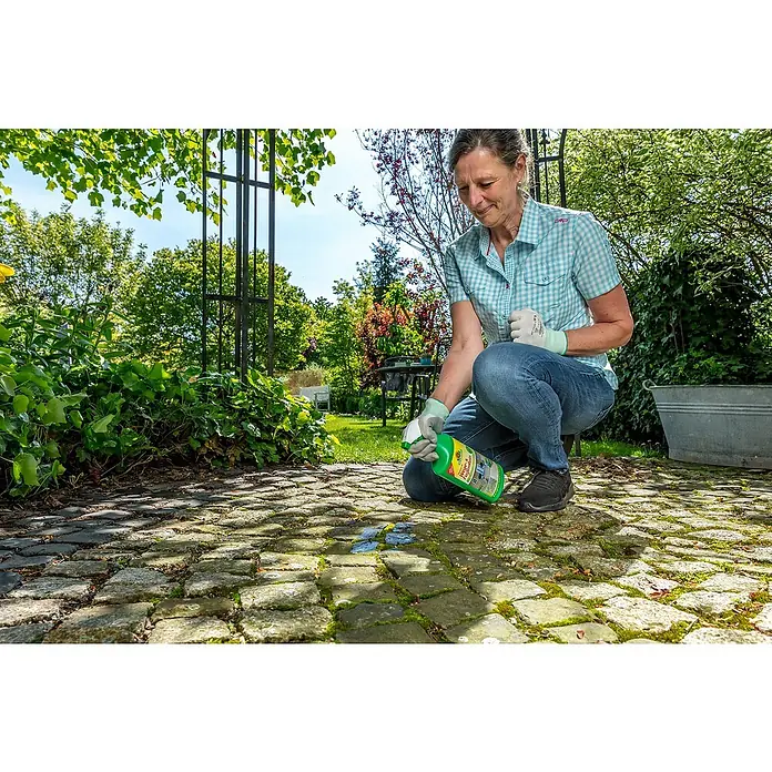 Neudorff Finalsan Wege- & Fugenrein - 1.000 ml, Sprühflasche - Eine Frau sprüht Moos Entferner auf ein Pflaster. Das Produkt ist in einer grünen Flasche mit weißer Sprühdüse abgefüllt.