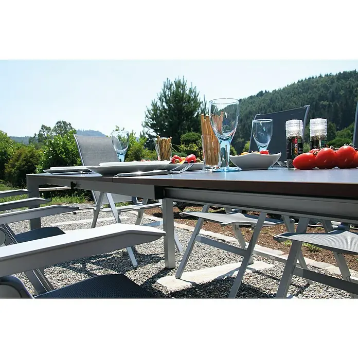 Acamp Gartenmöbel-Set Urban/Extensio - 7 -tlg., Aluminium, HPL, Textil, Silber - Ein Gartentisch mit Geschirr und Gläsern steht bereit für ein Essen im Freien, umgeben von grüner Natur.