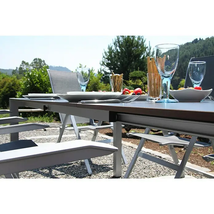 Acamp Gartenmöbel-Set Urban/Extensio - 5 -tlg., Aluminium, HPL, Textil, Klappbar, Anthrazit - Nahaufnahme eines Gartentisches mit Geschirr, Gläsern und Snacks. Der Tisch ist mit Stühlen umgeben, und im Hintergrund ist üppiges Grün zu sehen.