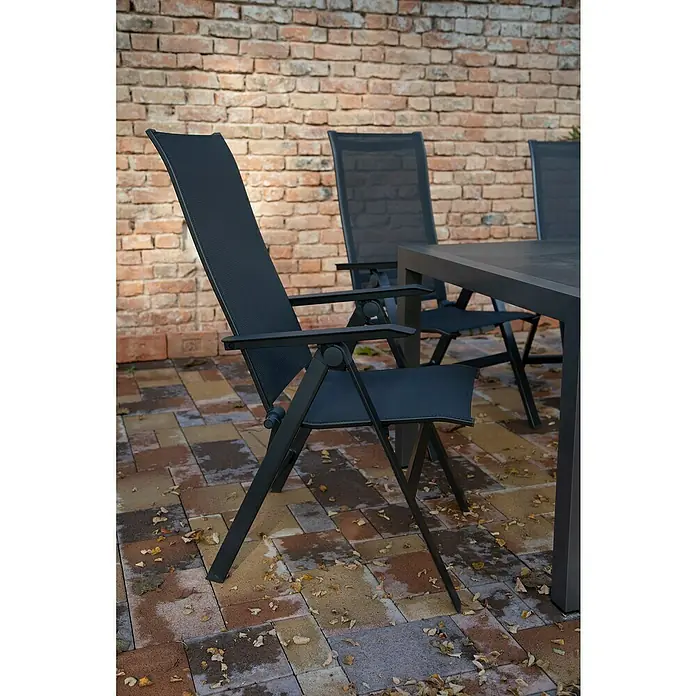 Acamp Gartenmöbel-Set Urban - 5 -tlg., Aluminium, HPL, Acatex, Rückenlehne verstellbar, Anthrazit - Ein verstellbarer Gartenstuhl aus Metall mit Textilbespannung steht auf einer gepflasterten Terrasse vor einer Backsteinmauer.