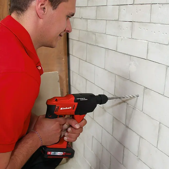 Einhell Power X-Change 18V Akku-Bohrhammer TE-HD 18 Li-Solo - 18 V, Ohne Akku - Ein Mann bohrt mit einem Einhell Akku-Betonbohrer in eine Ziegelwand. Das Werkzeug ist rot und schwarz und verfügt über einen starken Akku.