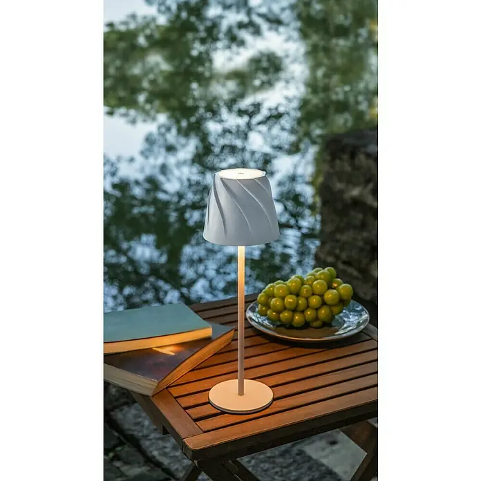 Starlux Akku-Tischleuchte Loreo - 4 W, L x B x H: 11 x 11 x 36 cm, Weiß, Warmweiß - Nahaufnahme einer modernen Tischleuchte neben einem Buch und einer Traube auf einem Holztisch im Freien.