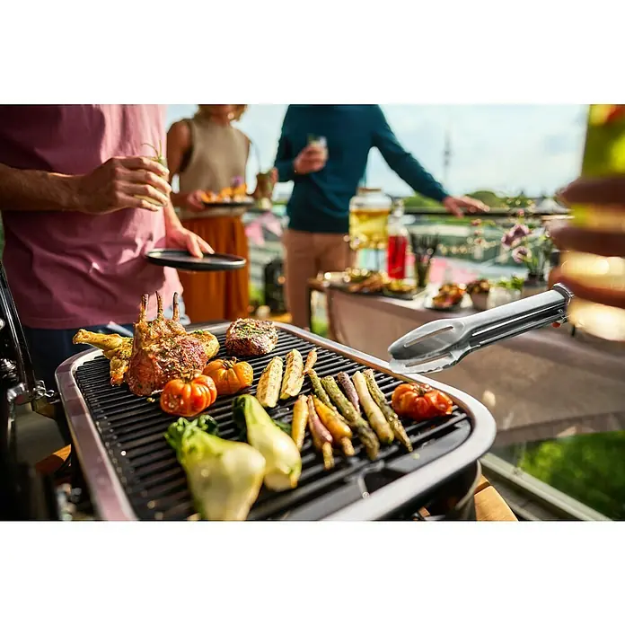 Weber Elektrogrill Lumin - Grillfläche (B x T): 49 x 33 cm, 2.200 W, Mintgrün - Ein elektrischer Grill im Freien mit Gemüse und Fleisch, während Leute im Hintergrund Getränke genießen.