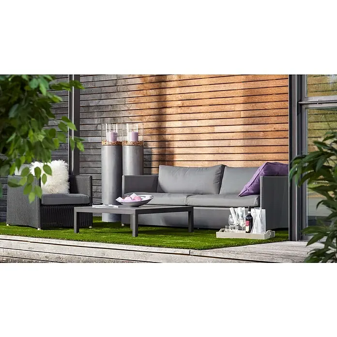Kunstrasen Olympic - 300 x 133 cm, Grün - Eine graue Couch und ein Sessel mit Tisch stehen auf einer Terrasse mit Holzwand. Dekorative Säulen und ein Serviertablett mit Getränken ergänzen die Szene.