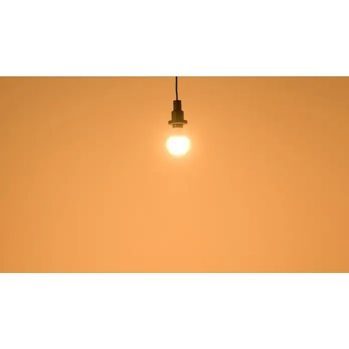 Ledvance Smart+ WiFi Smart-LED-Lampe Classic - E27, Neutralweiß, 1.055 lm, 9,5 W, Farbtemperatur einstellbar: Stufen - Nahaufnahme einer einzelnen Glühbirne, die von der Decke hängt und warmes Licht in einem Raum mit einem pfirsichfarbenen Hintergrund ausstrahlt.