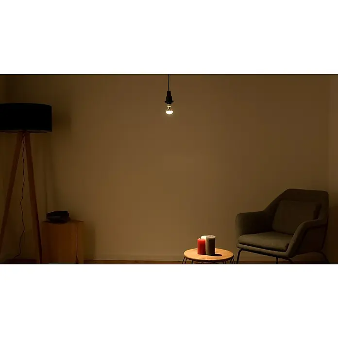 Osram Star LED-Lampe - E14, Nicht Dimmbar, Kaltweiß, 210 lm, 2,6 W - Eine Innenaufnahme zeigt eine Stehlampe, eine einzelne Glühbirne, einen Sessel und einen kleinen Tisch mit Kerzen, alles in warmem Licht.