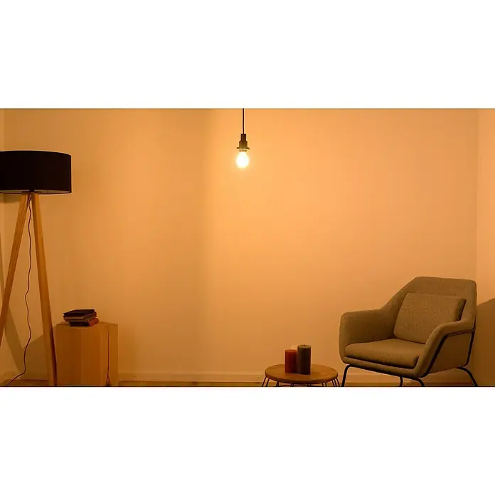 Osram LED-Lampe Glühlampenform E27 klar - E27, Nicht Dimmbar, Warmweiß, 806 lm, 7 W - Gemütliche Inneneinrichtung mit Stehlampe, Glühbirne, Sessel und Beistelltisch mit Kerzen, die eine warme Atmosphäre schaffen.