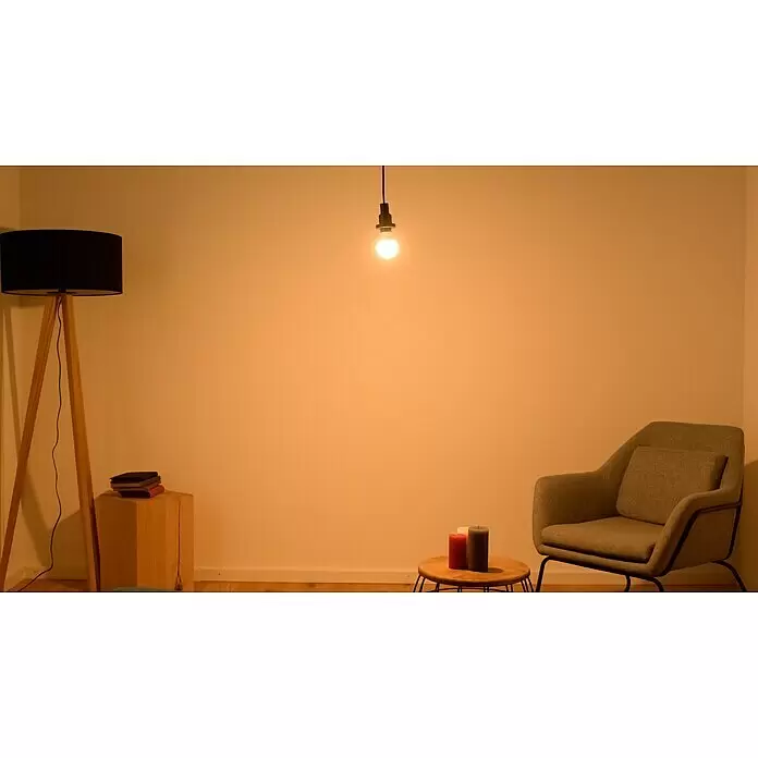 Osram LED-Lampen Set Glühlampenform E27 matt - E27, Nicht Dimmbar, Warmweiß, 806 lm, 9 W, 5 Stk. - Minimalistisches Zimmer mit hängender Glühbirne, Stehlampe, Sessel und Kerzen auf einem Holztisch, alles in warmem Licht.