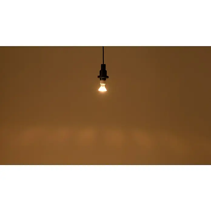Osram LED-Lampe Reflektor GU10 - GU10, Dimmbar, Warmweiß, 350 lm, 5,5 W - Eine einzelne, glühende Glühbirne hängt von der Decke und spendet warmes Licht in dem ansonsten dunklen Raum.