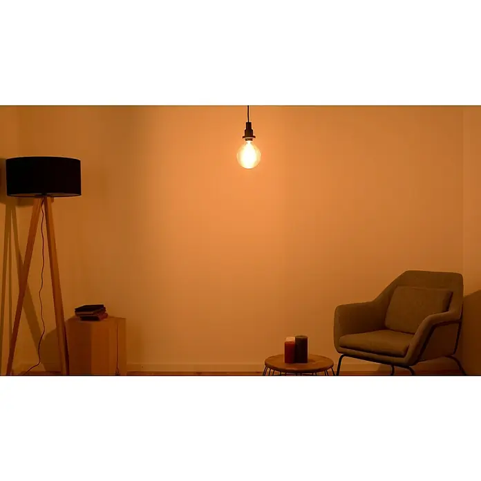 Osram LED-Lampe Vintage Edition 1906 Globe-Form E27 - E27, Nicht Dimmbar, Warmweiß, 725 lm, 7 W, Globe - Zimmerinterieur mit Stehlampe, Sessel und Glühbirne, die eine gemütliche Atmosphäre schaffen. Warmes Licht erhellt den Raum und betont das minimalistische Design.