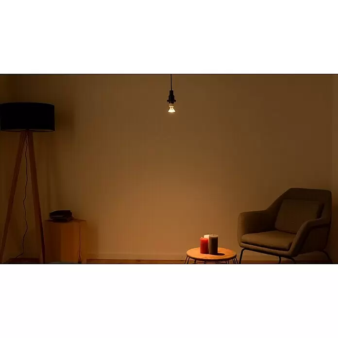 Osram Star LED-Lampen Set Reflektor GU10 - GU10, Nicht Dimmbar, Warmweiß, 230 lm, 2,6 W, 3 Stk. - Eine nackte, warm leuchtende Glühbirne hängt zentral und beleuchtet einen gemütlichen Raum mit Stuhl, Stehlampe und Kerzen.