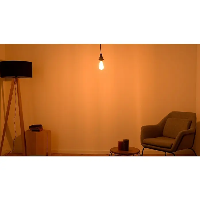 Osram LED-Lampe Vintage Edition 1906 Birnenform E27 - E27, Dimmbar, Warmweiß, 470 lm, 5,9 W, Gold - Gemütliche Leseecke mit Stehlampe, Deckenleuchte, Sessel und Beistelltisch mit Kerzen und Büchern in warmem Licht.