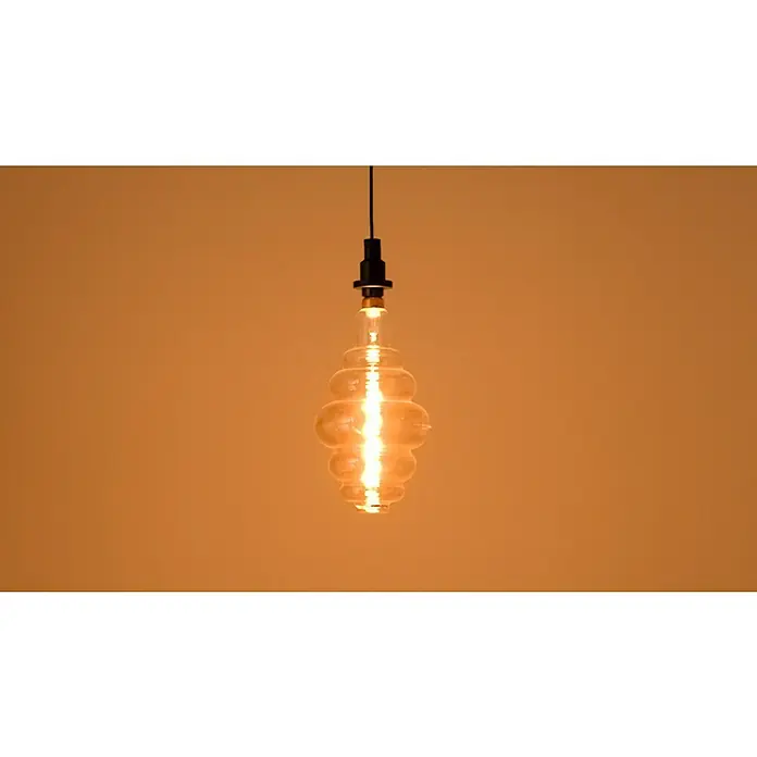 Osram LED-Lampe Vintage Edition 1906 Glühlampenform E27 - E27, Dimmbar, Warmweiß, 360 lm, 4,8 W - Eine dekorative Glühbirne mit einzigartiger Form hängt an einem Kabel und strahlt warmes Licht in einem sanften, orangefarbenen Farbton aus.