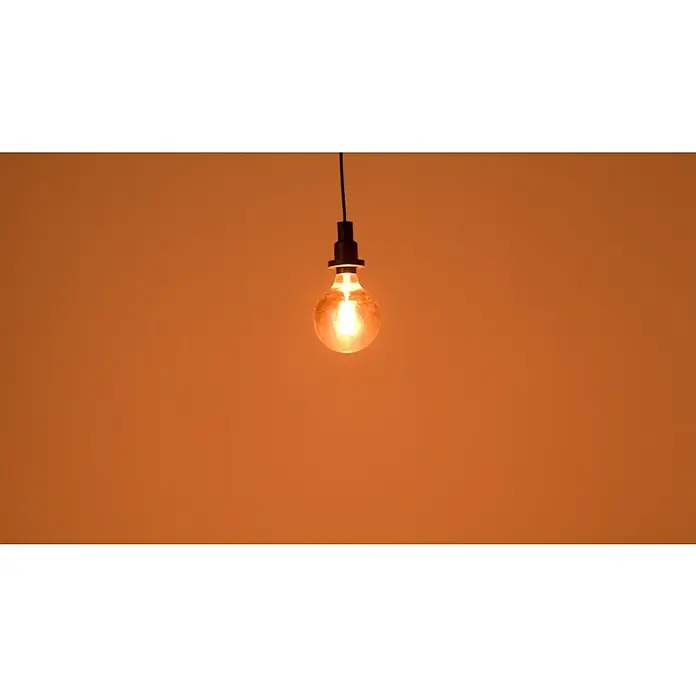 Osram LED-Lampe Vintage Edition 1906 Globe-Form E27 - Durchmesser: 12,4 cm, E27, Dimmbar, Warmweiß, 360 lm, 7,8 W - Nahaufnahme einer einzelnen, hängenden Glühbirne mit warmem Licht, die an einer schwarzen Fassung und einem Kabel befestigt ist.