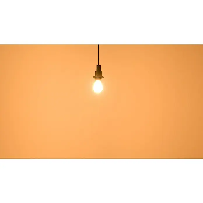 Osram LED-Lampe Osram LED-Lampe Glühlampenform E27 matt mit Tageslichtsensor - E27, Nicht Dimmbar, Warmweiß, 806 lm, 7,3 W - Helle, leuchtende Glühbirne an einem schwarzen Kabel. Die minimalistische Lampe hängt vor einem einfarbigen orangefarbenen Hintergrund.