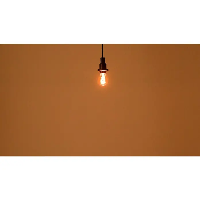 Osram LED-Lampe Vintage Edition 1906 Glühlampenform E27 - E27, Nicht Dimmbar, Warmweiß, 100 lm, Birne, Smoke - Glühbirne hängt an einem Kabel vor einer braunen Wand, erzeugt warmes Licht und eine gemütliche Atmosphäre im Raum.