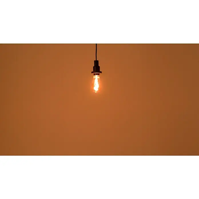 Osram LED-Lampe Vintage Edition 1906 Birnenform E27 - E27, Nicht Dimmbar, Warmweiß, 100 lm, 3,5 W, Smoke - Glühende Edison-Glühbirne mit schwarzer Fassung hängt vor einem monochromen Hintergrund und strahlt warmes Licht aus.